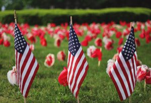 Labor Day: three American Flags in the ground with flowers behind